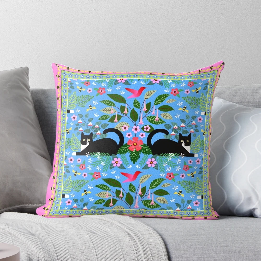 Tuxedo cat resting on a pillow with a hummingbird design