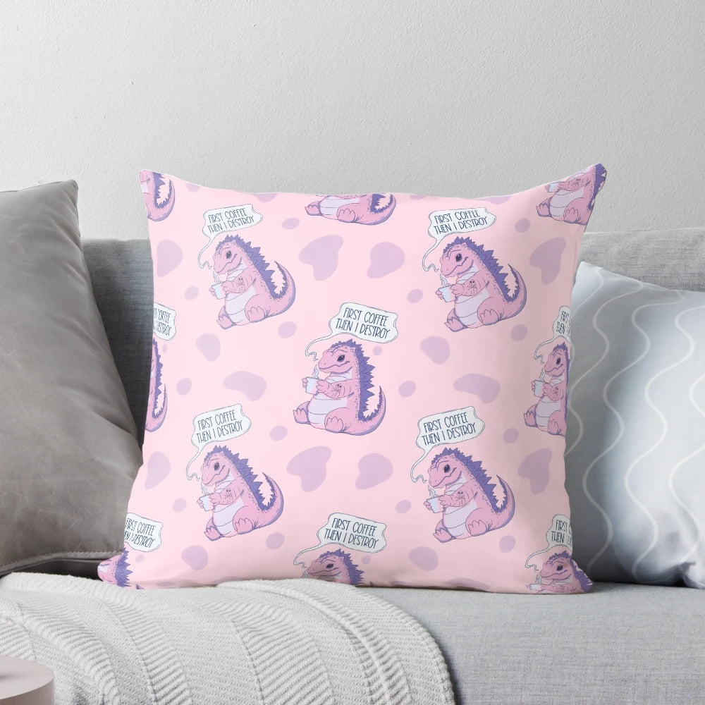 A pastel pink pillow with a playful dinosaur-like monster character and the text "First coffee then I destroy" printed on it.