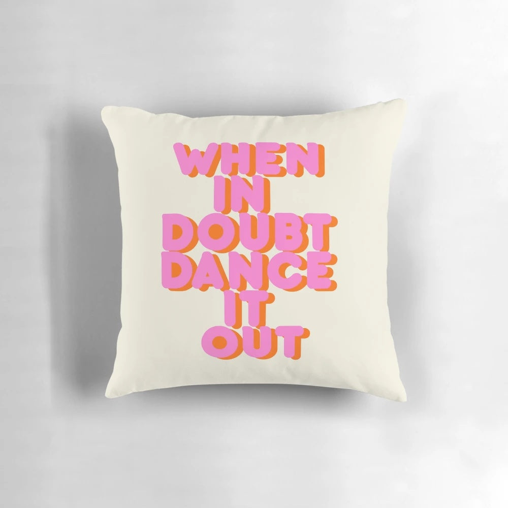 A white throw pillow with bold and vibrant "When in Doubt, Dance It Out!" typography artwork in shades of pink.