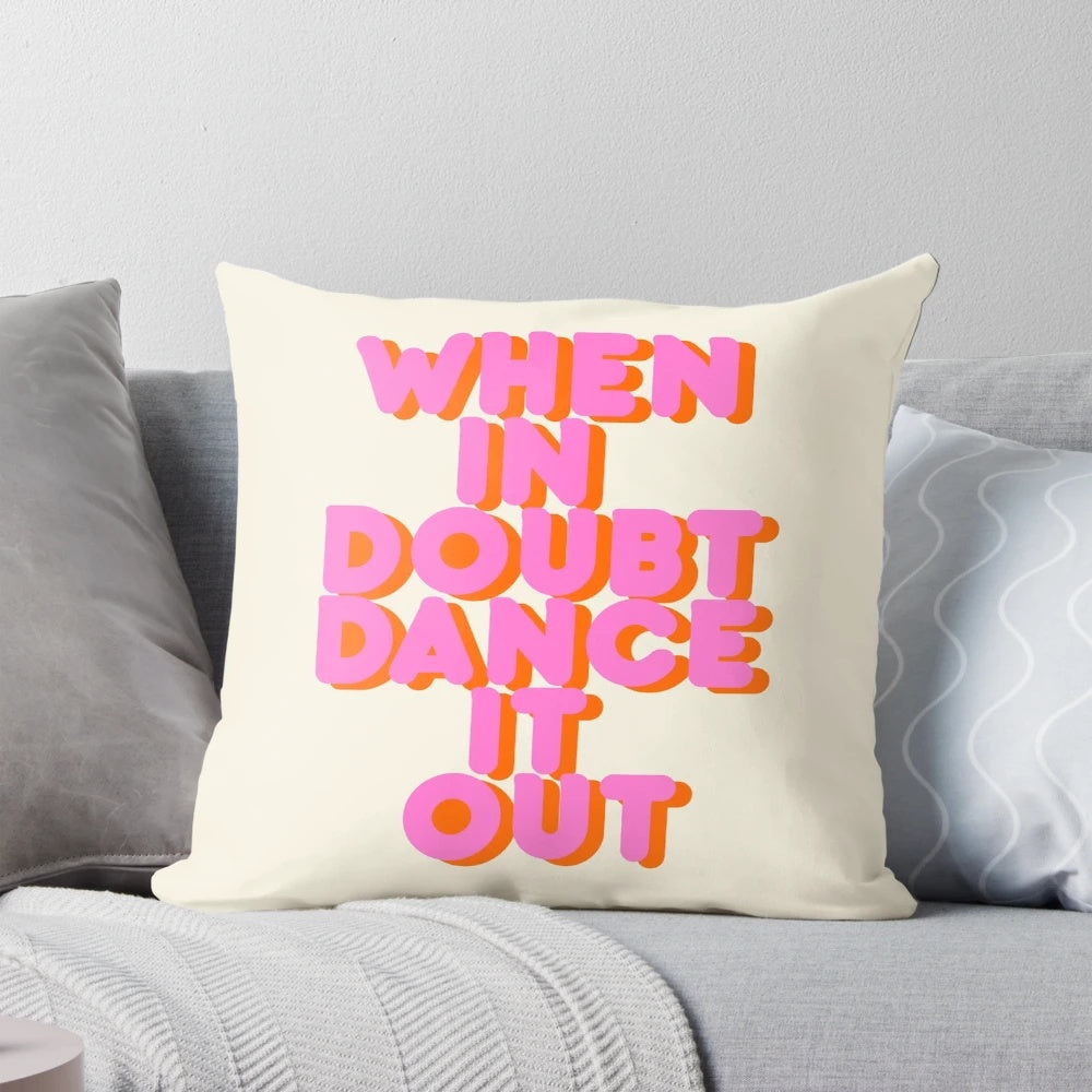 A white throw pillow with bold and vibrant "When in Doubt, Dance It Out!" typography artwork in shades of pink.