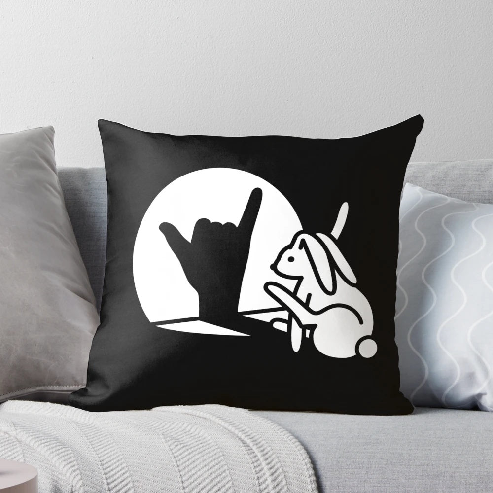 Photograph of a decorative pillow featuring a rabbit shadow hand making the 'Call You' hand sign from sign language.