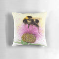 Closeup of a beautiful watercolor painting of a bee perched on a purple thistle flower, presented on a decorative throw pillow.