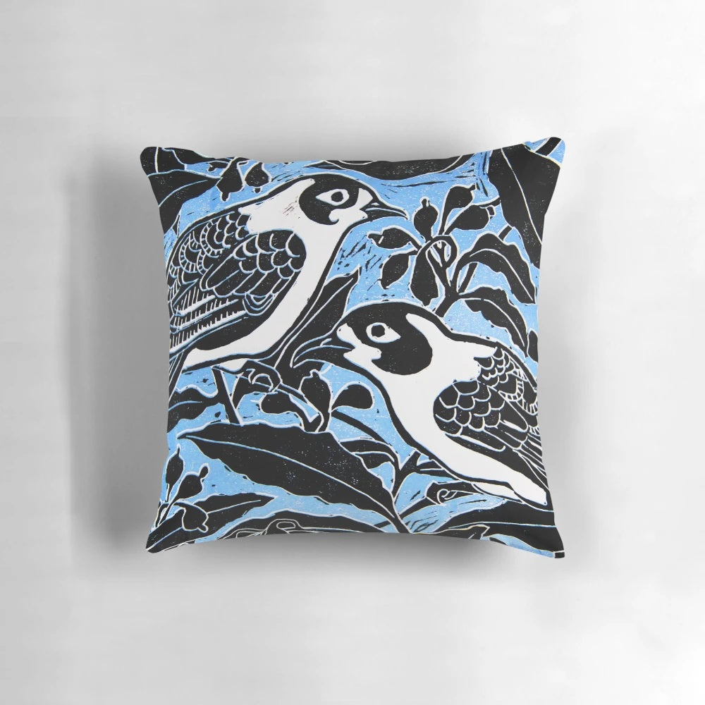 A beautiful throw pillow featuring a linocut-inspired image of blue birds perched on a tree branch with flowers and leaves.
