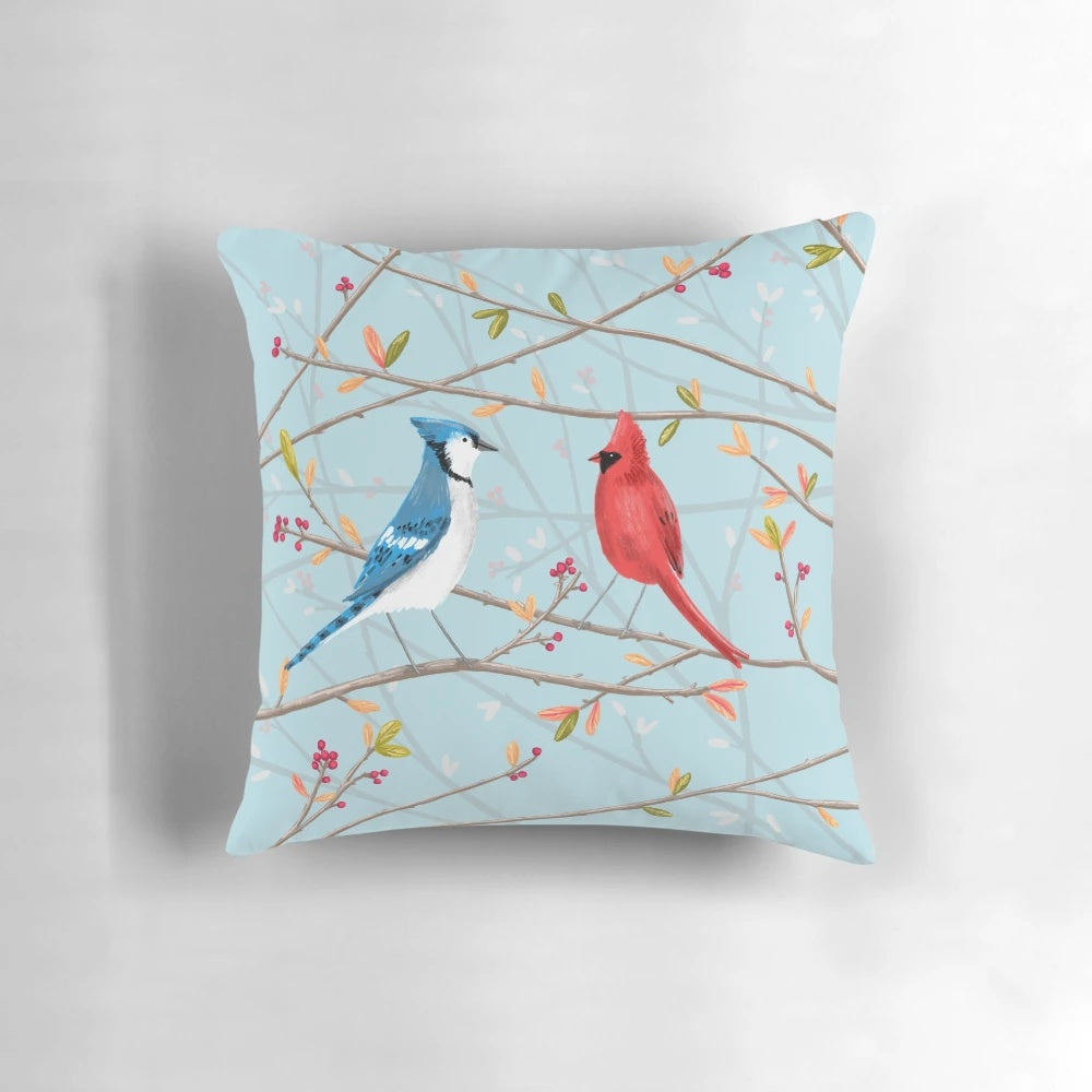 A colorful throw pillow featuring a seamless pattern of blue jays and red cardinals perched on tree twigs.
