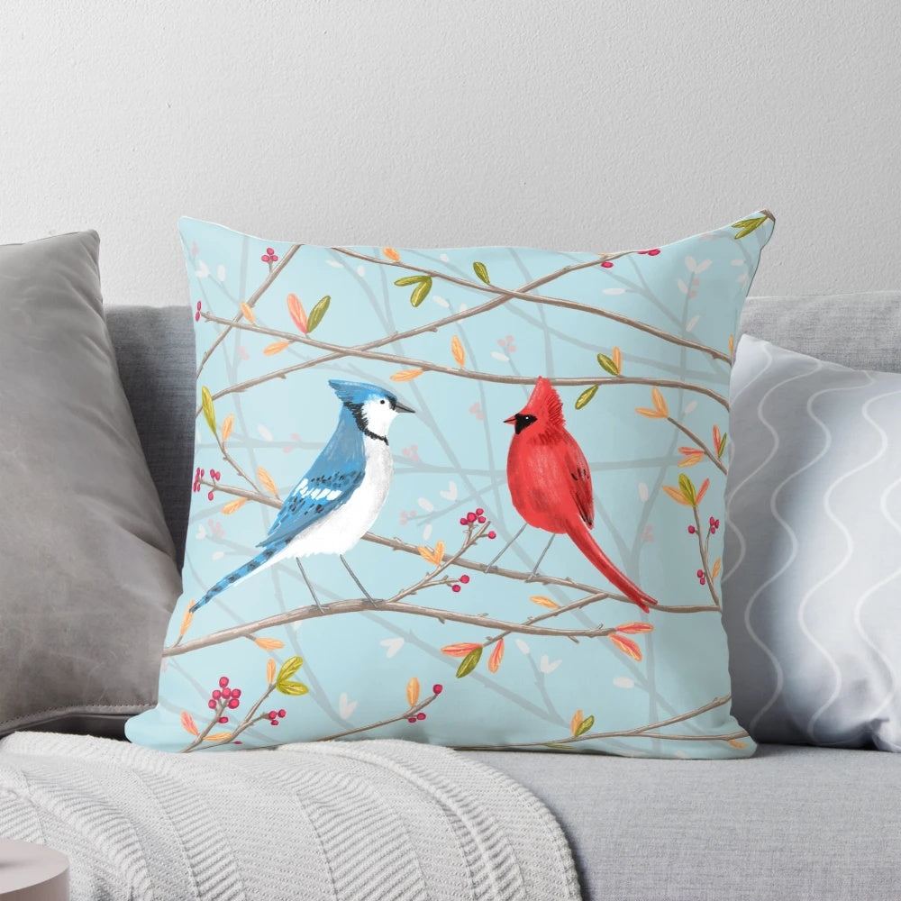 A colorful throw pillow featuring a seamless pattern of blue jays and red cardinals perched on tree twigs.