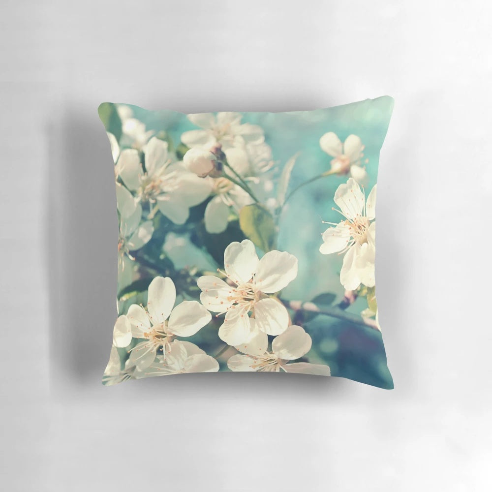 A soft, decorative pillow featuring a close-up image of delicate pink cherry blossoms on a tree branch.