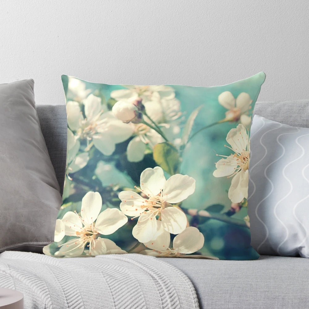 A soft, decorative pillow featuring a close-up image of delicate pink cherry blossoms on a tree branch.