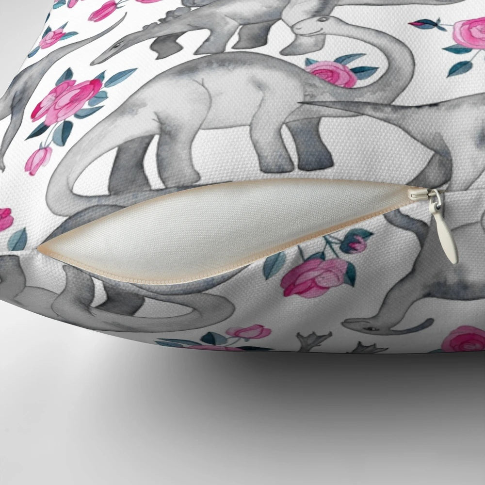 Pillow featuring a watercolor design of dinosaurs and roses in white, pink, and shades of green.