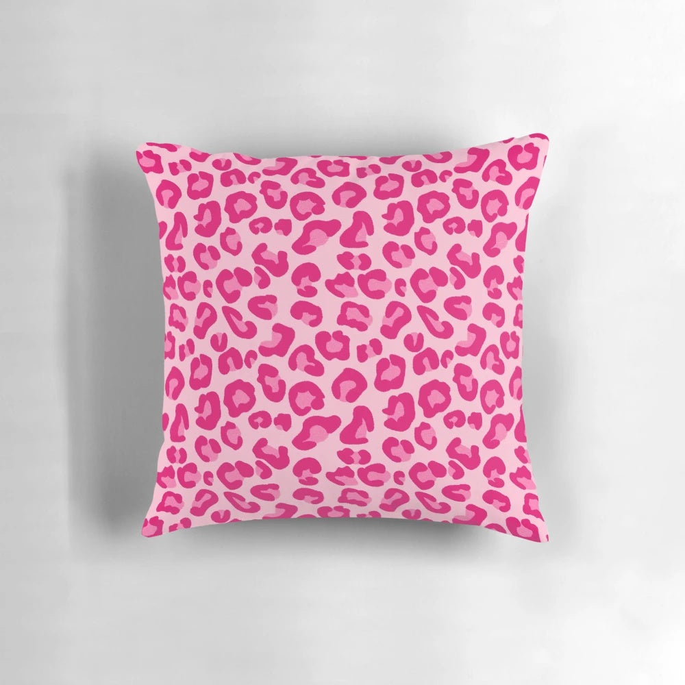 A plush, rectangular pillow with a modern leopard print design in shades of pink and fuchsia.