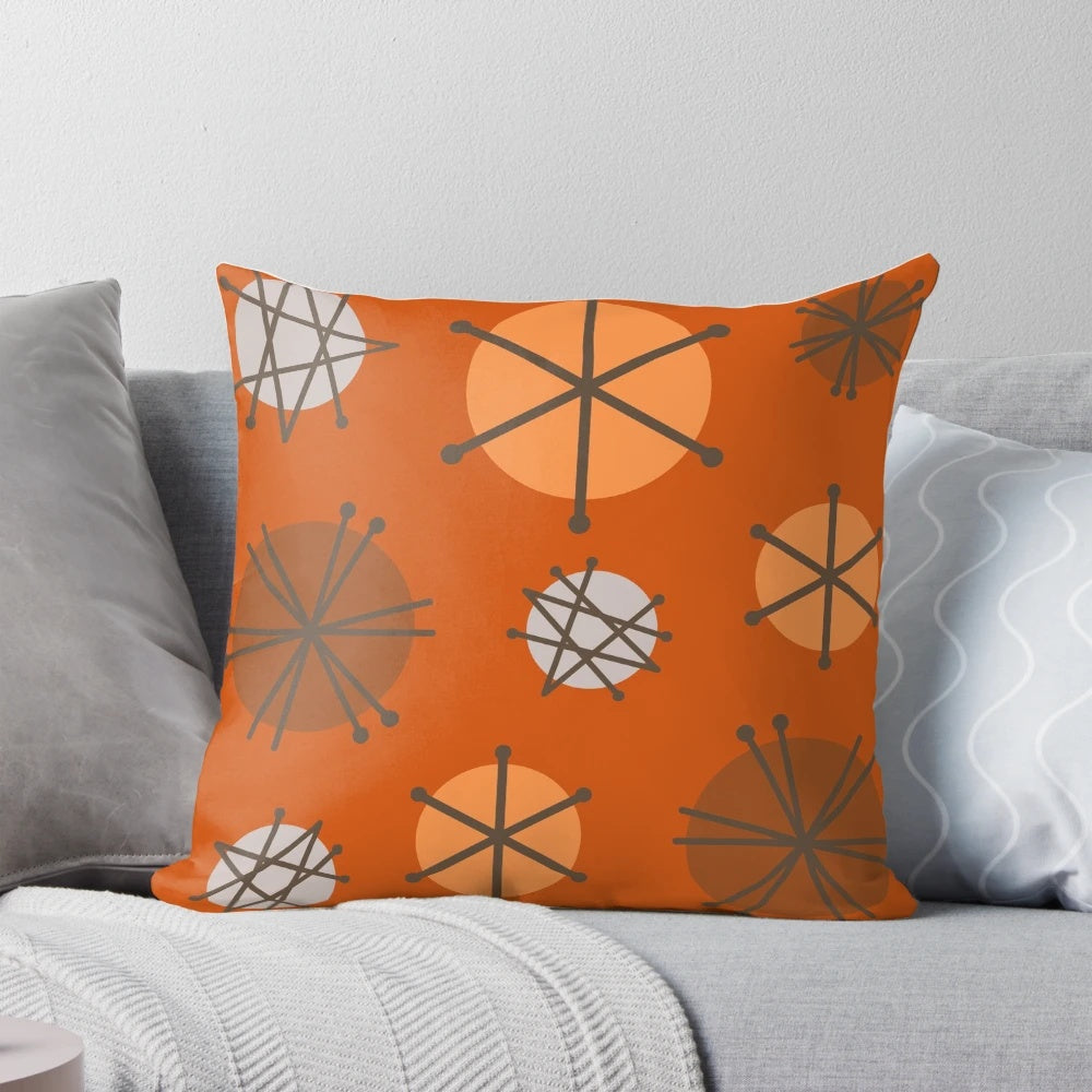 An orange pillow featuring a vibrant mid century modern starburst pattern, reflecting the 20th century space age aesthetic.