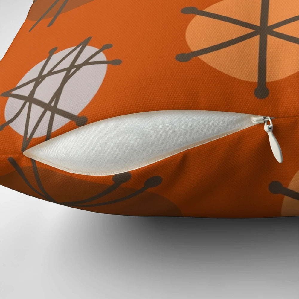 An orange pillow featuring a vibrant mid century modern starburst pattern, reflecting the 20th century space age aesthetic.