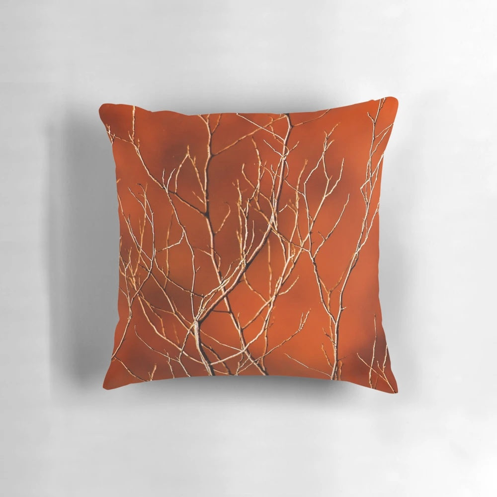 Vibrant orange pillow with a high-contrast design of bare, dark branches against a fiery background.