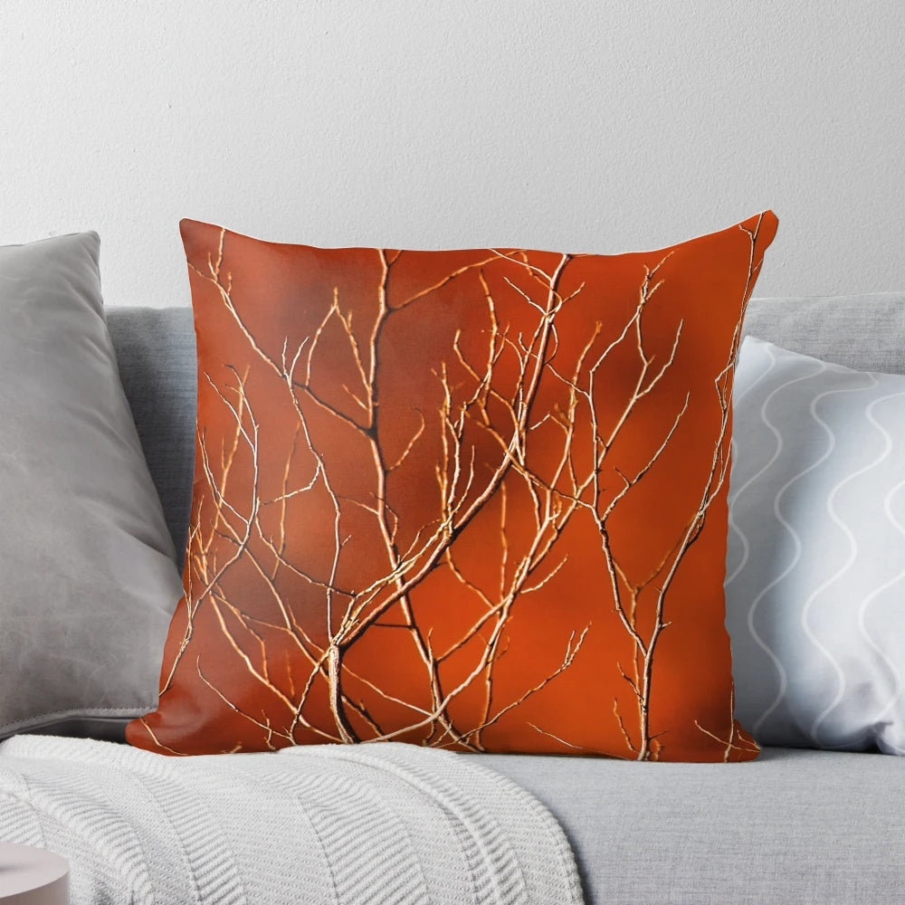 Vibrant orange pillow with a high-contrast design of bare, dark branches against a fiery background.