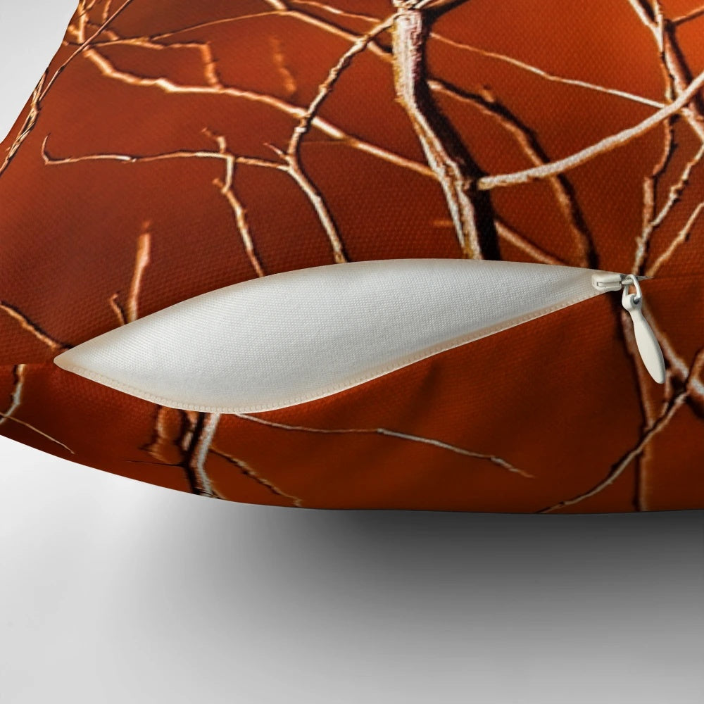 Vibrant orange pillow with a high-contrast design of bare, dark branches against a fiery background.