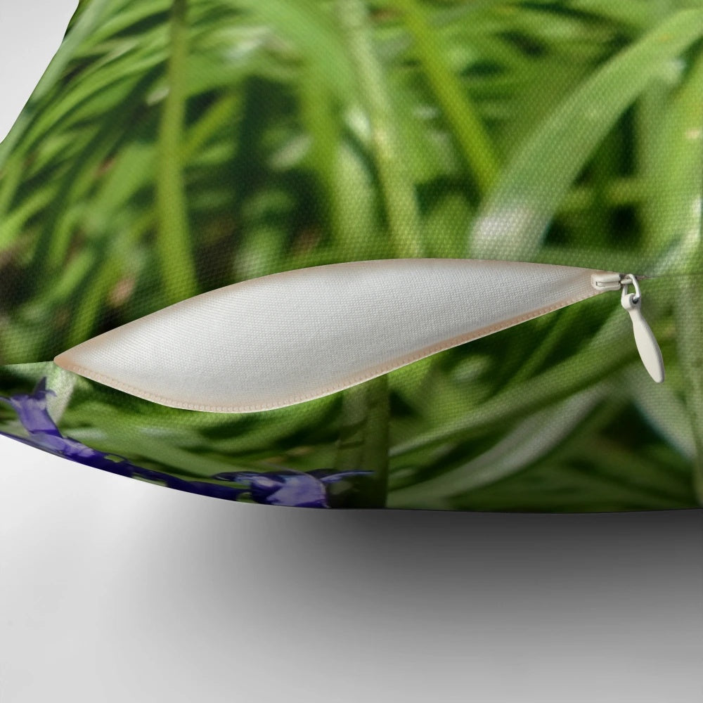 A decorative pillow featuring a vibrant peacock butterfly perched on a bed of blooming bluebells in a lush, wild woodland scene.