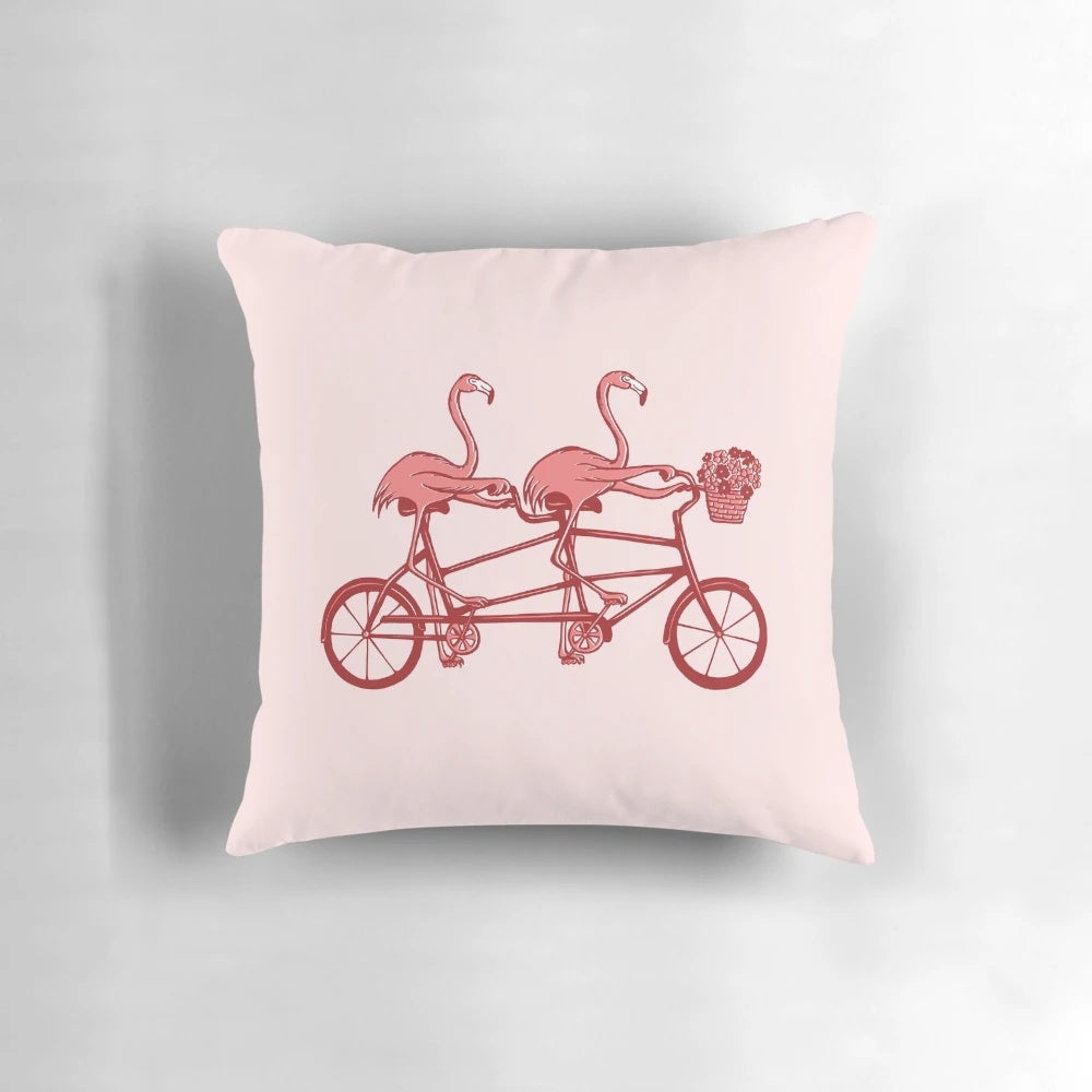 Colorful pink flamingos riding a tandem bicycle on a decorative pillow