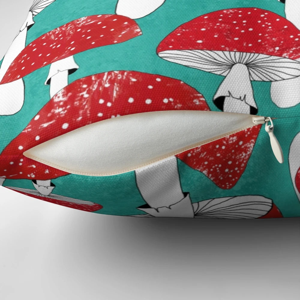 Artistic illustration of red mushrooms on a turquoise blue background, featured on a decorative pillow.