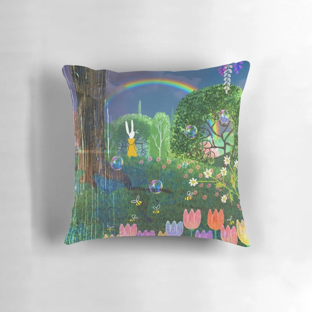 A colorful spring-themed pillow featuring bunnies, flowers, and a rainbow against a lush, green background.