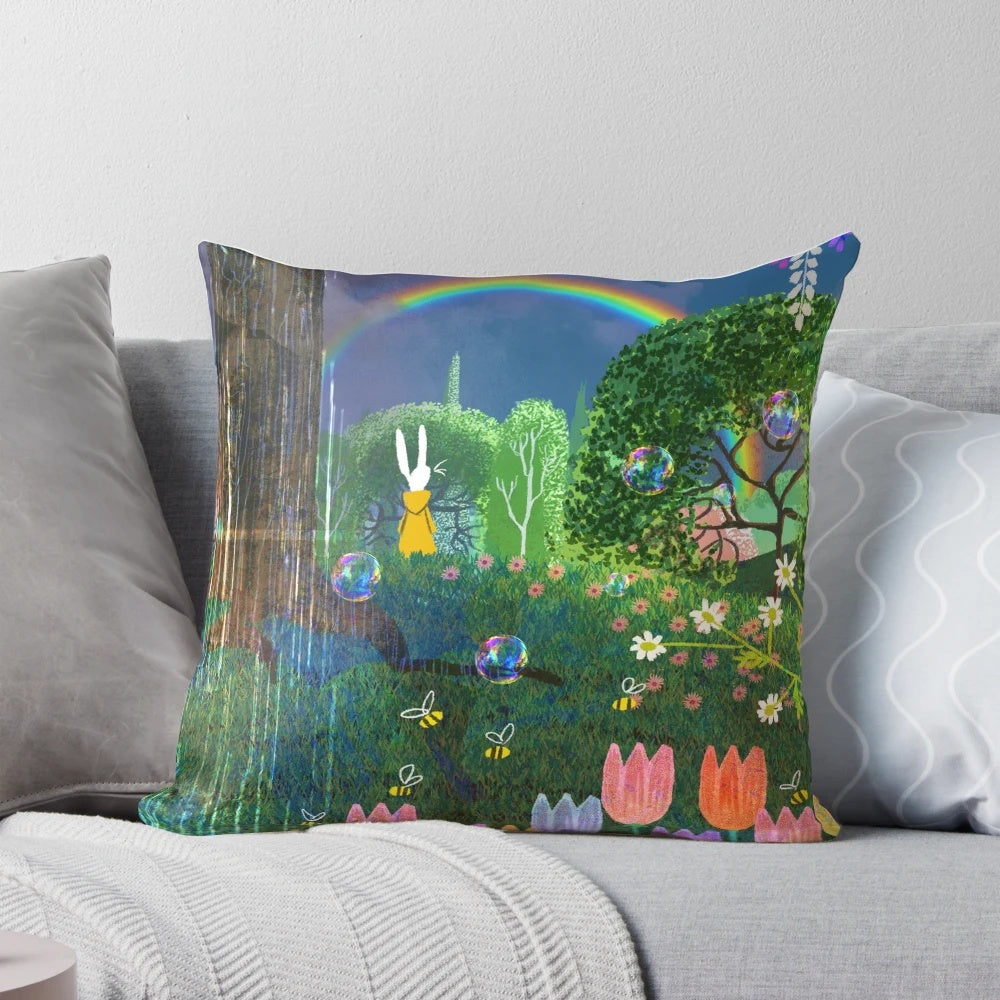 A colorful spring-themed pillow featuring bunnies, flowers, and a rainbow against a lush, green background.