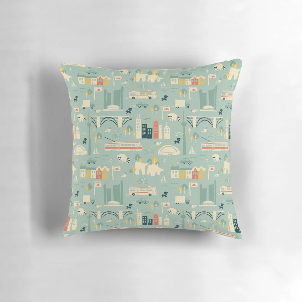 Decorative square pillow featuring a vibrant cityscape of Toronto's iconic buildings, buses, and streetcars.