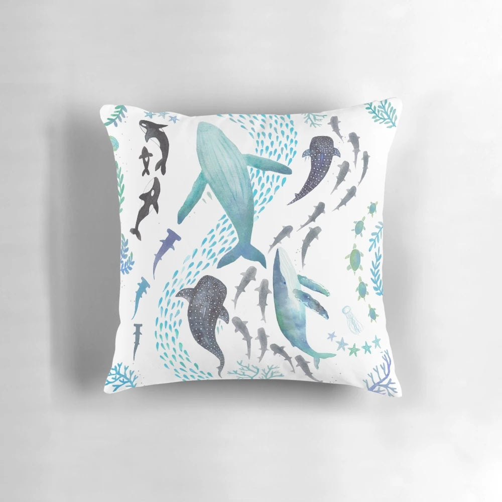 Colorful throw pillow featuring a watercolor design of sharks, whales, orcas, and sea turtles swimming in the ocean.