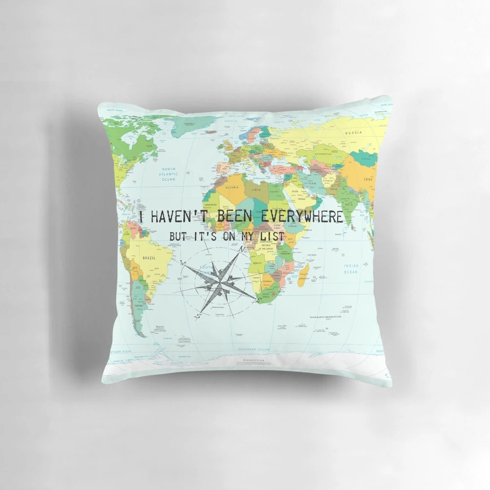 A throw pillow featuring the travel quote "I haven't been everywhere but it's on my list" with a compass rose and world map design.