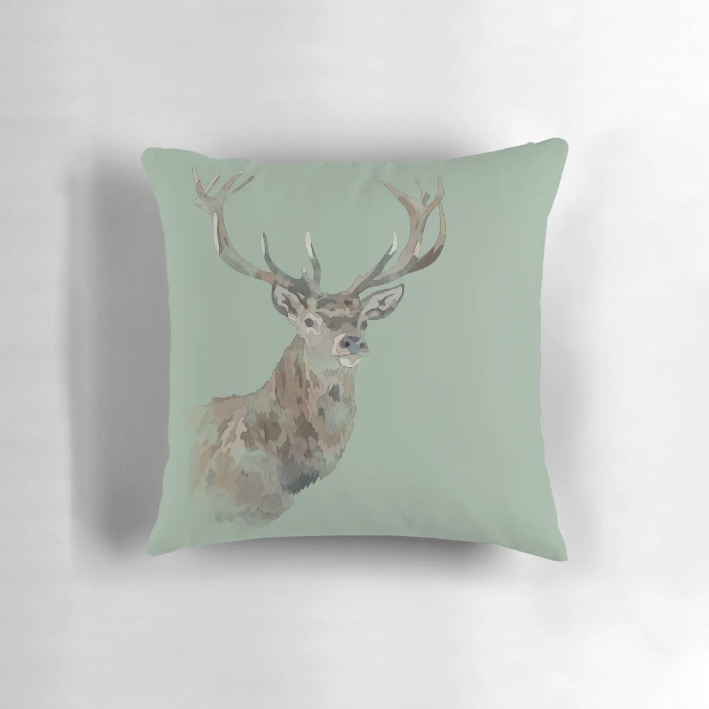 A watercolor-style illustration of a majestic stag with antlers set against a green woodland background on a throw pillow.