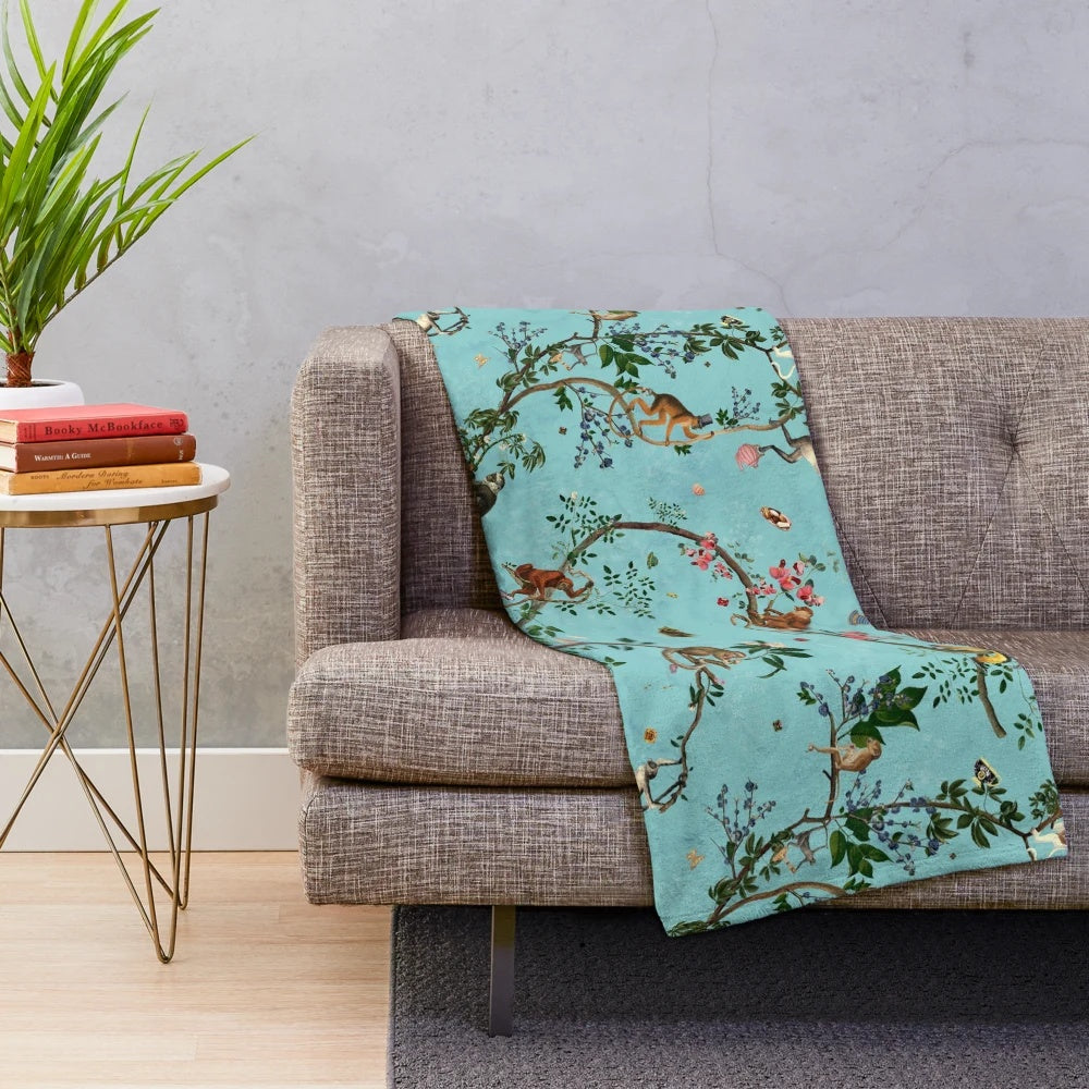 Soft and plush aqua-colored blanket with playful monkey and jungle plant designs