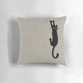 A playful black cat clinging to a pillow with its sharp claws