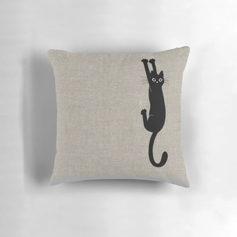 A playful black cat clinging to a pillow with its sharp claws