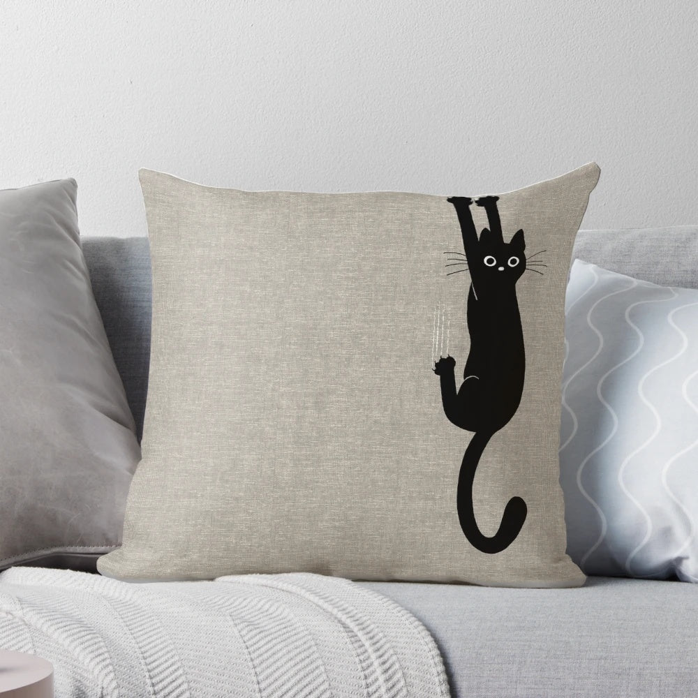 A playful black cat clinging to a pillow with its sharp claws