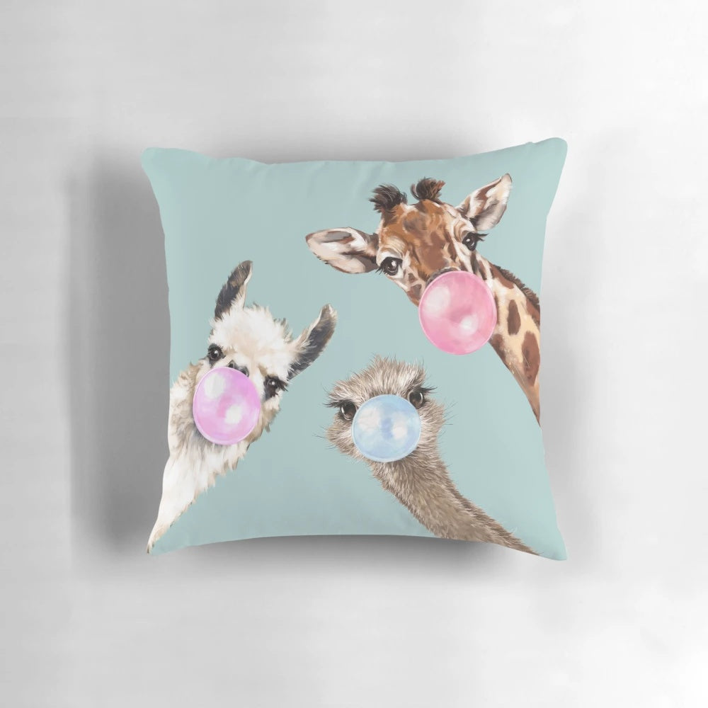 Colorful illustration of a bubble gum-chewing llama, ostrich, and giraffe on a blue pillow