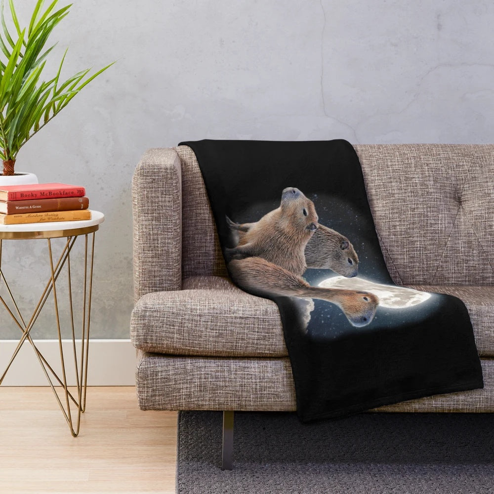 Adorable capybara characters sitting on a crescent moon against a starry night sky on a soft, cozy plush blanket