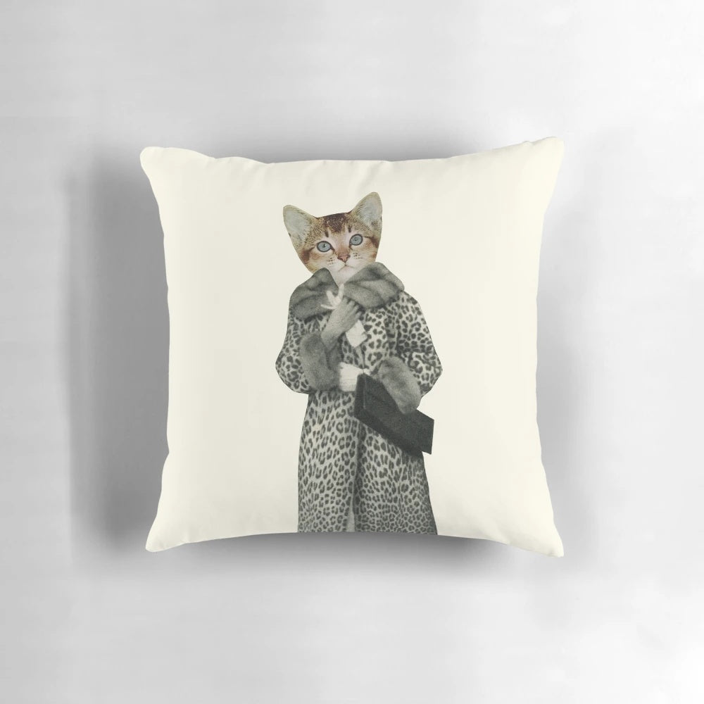A white and orange kitten wearing a leopard print dress and posing on a pillow