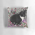 A whimsical pillow featuring a tuxedo cat surrounded by a colorful floral meadow
